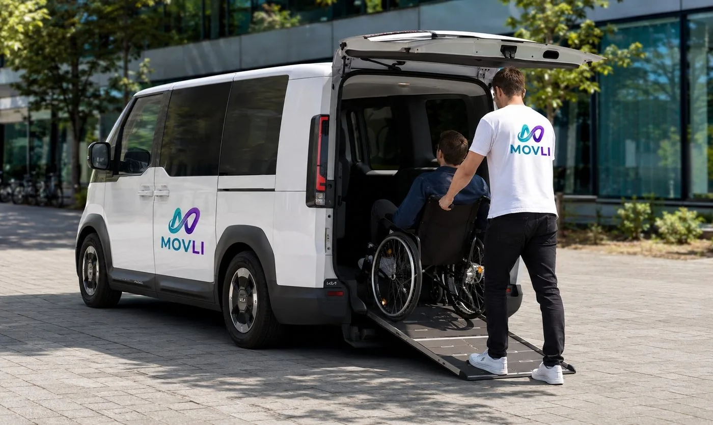 Movli Mitarbeiter begleitet einen Fahrgast im Rollstuhl über die Rampe in den weißen Movli Van
